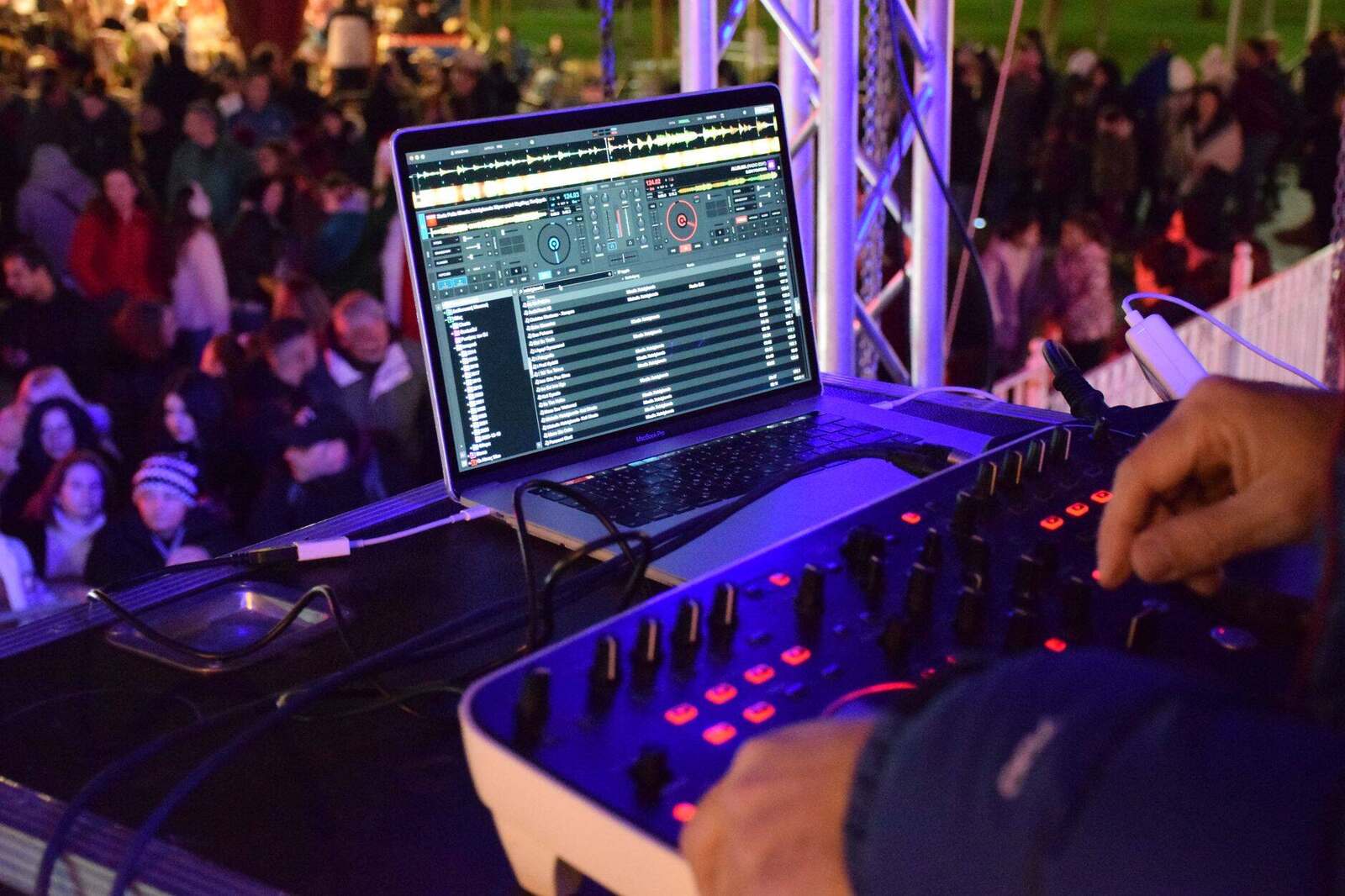 DJ running laptop show software at an outdoor night event with a crowd watching