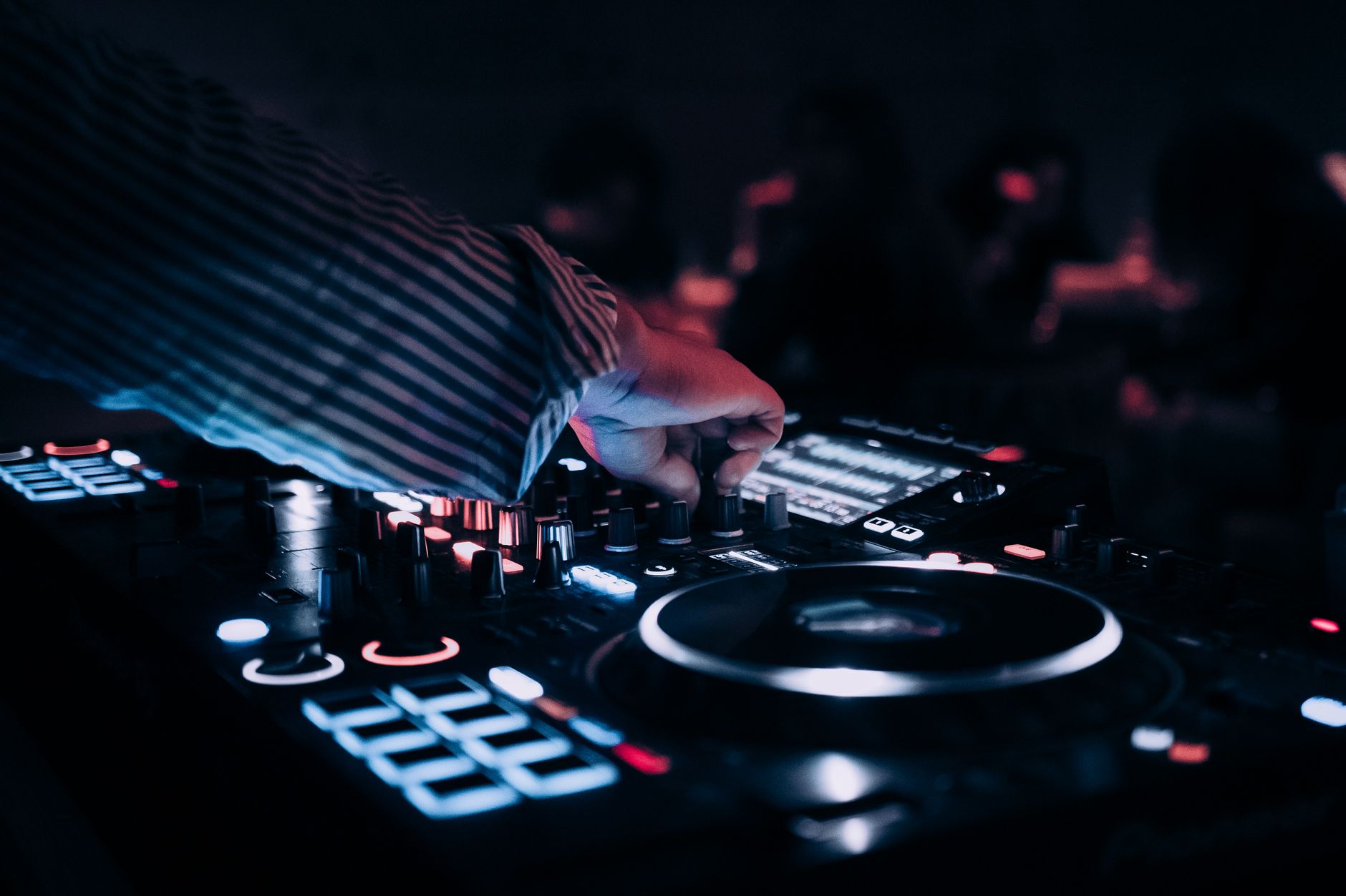 DJ mixing on CDJs in a dark club booth, hands on the jog wheel